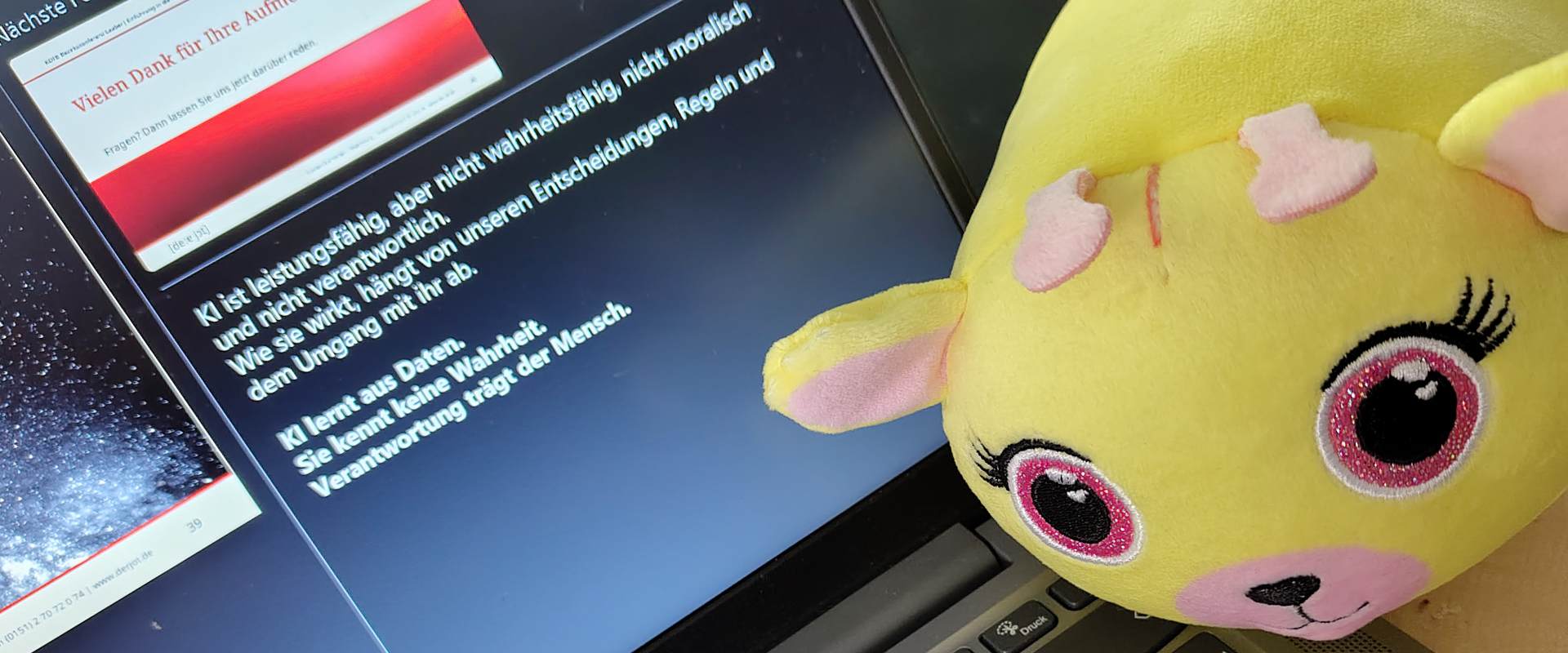 Plüschfigur vor Laptop mit Präsentationsfolie zu Künstlicher Intelligenz während eines Vortrags