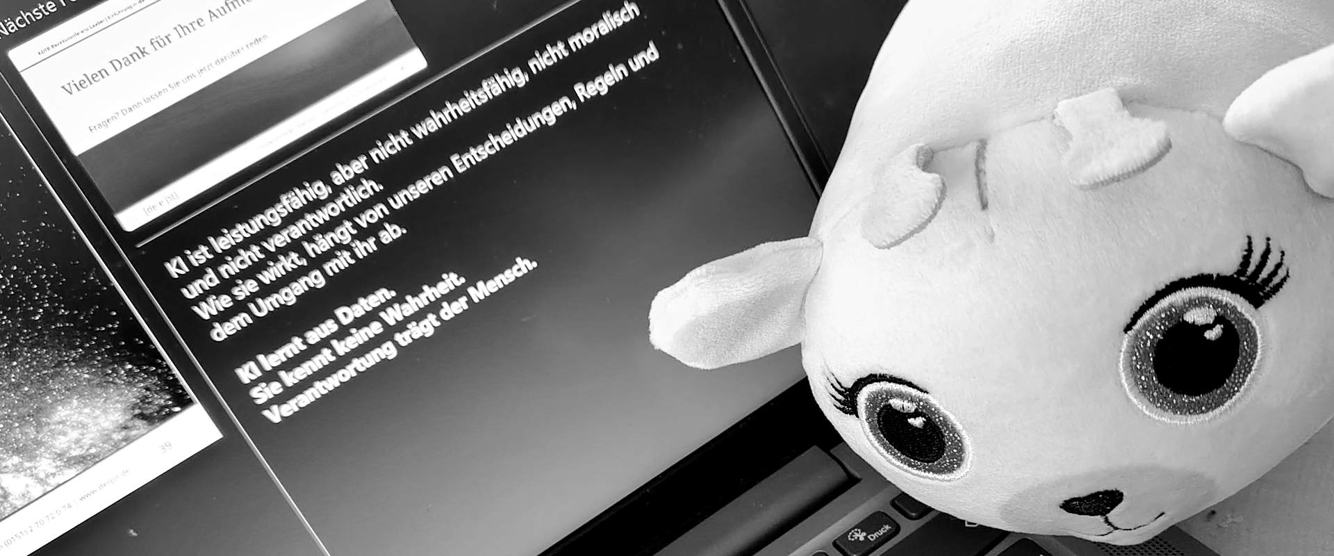 Plüschfigur vor Laptop mit Präsentationsfolie zu Künstlicher Intelligenz während eines Vortrags